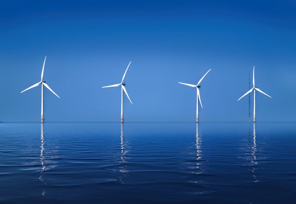 Serene landscape of offshore wind turbines reflecting on calm ocean water.
